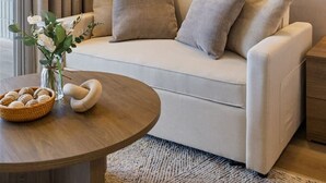 En moderne stue med en sofa, et rundt spejl, en vase med blomster og et bord med en kurv og en dekorativ genstand.