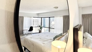 Une chambre d’hôtel avec un grand lit, une chaise, une petite table et une vue sur la ville grâce à de grandes fenêtres.