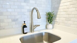 A modern kitchen with a stainless steel sink, white tiled backsplash, and a potted plant. - Stunning Mountain View Studio – High Floor Waikiki 3107B (Honolulu)