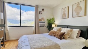 A bedroom with a large bed, a desk, a chair, a window with a view of the mountains, and wall decorations. - Stunning Mountain View Studio – High Floor Waikiki 3107B (Honolulu)
