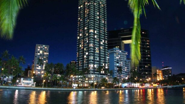 A nighttime cityscape with a prominent high-rise building reflecting on the water. - Stunning Mountain View Studio – High Floor Waikiki 3107B (Honolulu)