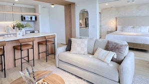 Una sala de estar moderna con un sofá, una mesa de centro y una cocina con microondas y taburetes de bar.