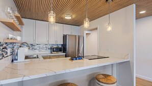 A modern kitchen with white cabinets, a marble countertop, stainless steel appliances, and wooden ceiling. - Waikiki Ocean Luxe Panorama 2BD, Free Parking (Honolulu)