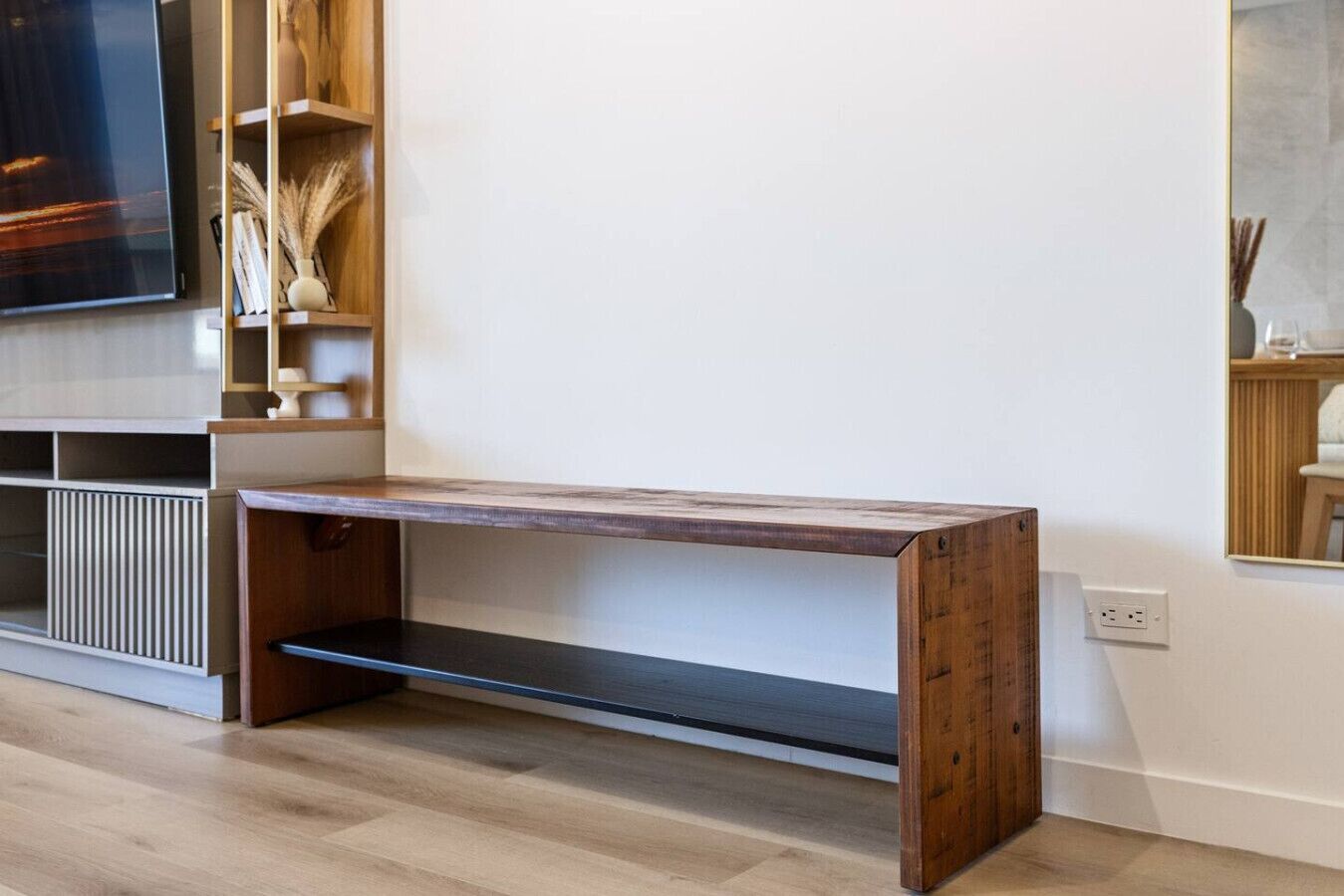 Una sala moderna con un banco de madera, un televisor de pantalla plana y una estantería empotrada con objetos decorativos.