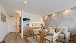 Eine moderne Küche mit weißen Schränken, einem Holztisch und einem grauen Sofa im Wohnbereich.