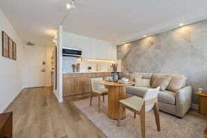 Eine moderne Küche mit weißen Schränken, einem Holztisch und einem grauen Sofa im Wohnbereich.