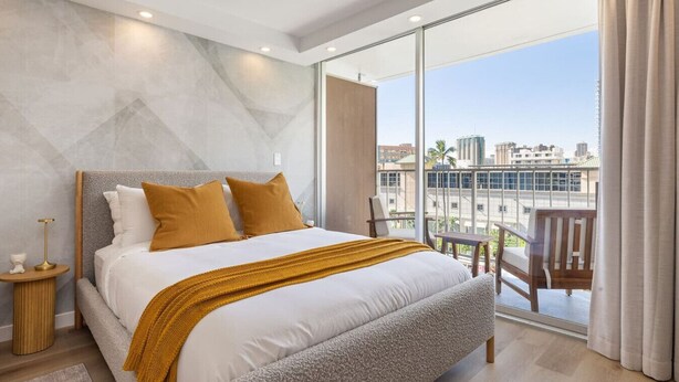 Ein modernes Schlafzimmer mit einem großen Bett, Blick auf die Stadt und einem Balkon mit einem Stuhl.
