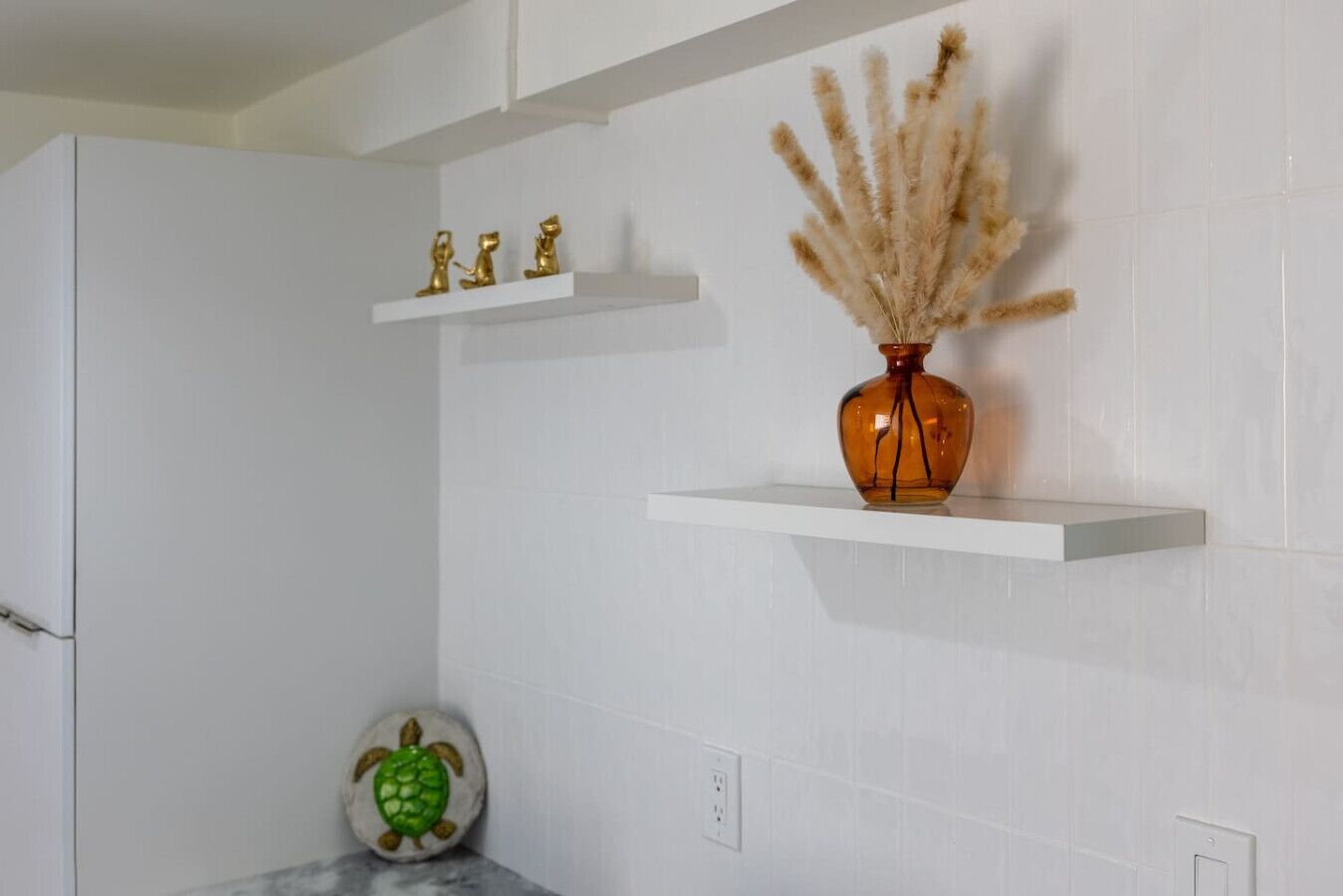 A bathroom with white tiles, a vase with dried plants, and a turtle decoration on the floor.