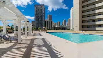 A pool area with lounge chairs and a city skyline in the background.