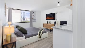 A modern bedroom with a bed, bedside table, lamp, TV, and a view of a cityscape through the window.