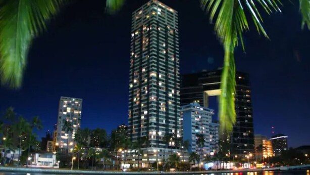 A nighttime cityscape with a prominent high-rise building reflecting on the water. - Waikiki Tranquil Retreat (Honolulu)