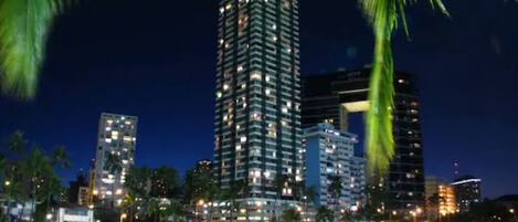A nighttime cityscape with a prominent high-rise building reflecting on the water.