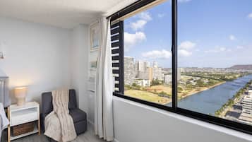 A modern room with a large window, a chair, a bedside table, and a lamp.