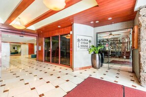 Een hotel lobby met een zwart-wit geruite vloer, een grote potplant en een bord dat Aloha Steak House aankondigt.