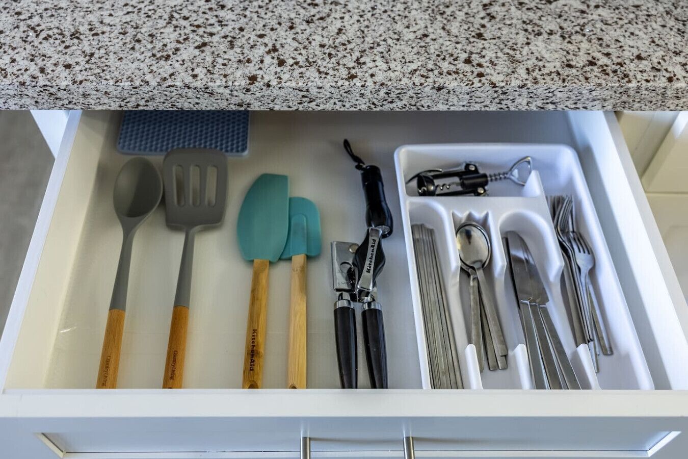 A kitchen drawer with various utensils including a spoon, spatula, spatula, and a can opener.