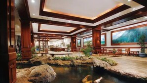 Vestíbulo de hotel con estanque de peces koi, mobiliario de madera y ventanas amplias.