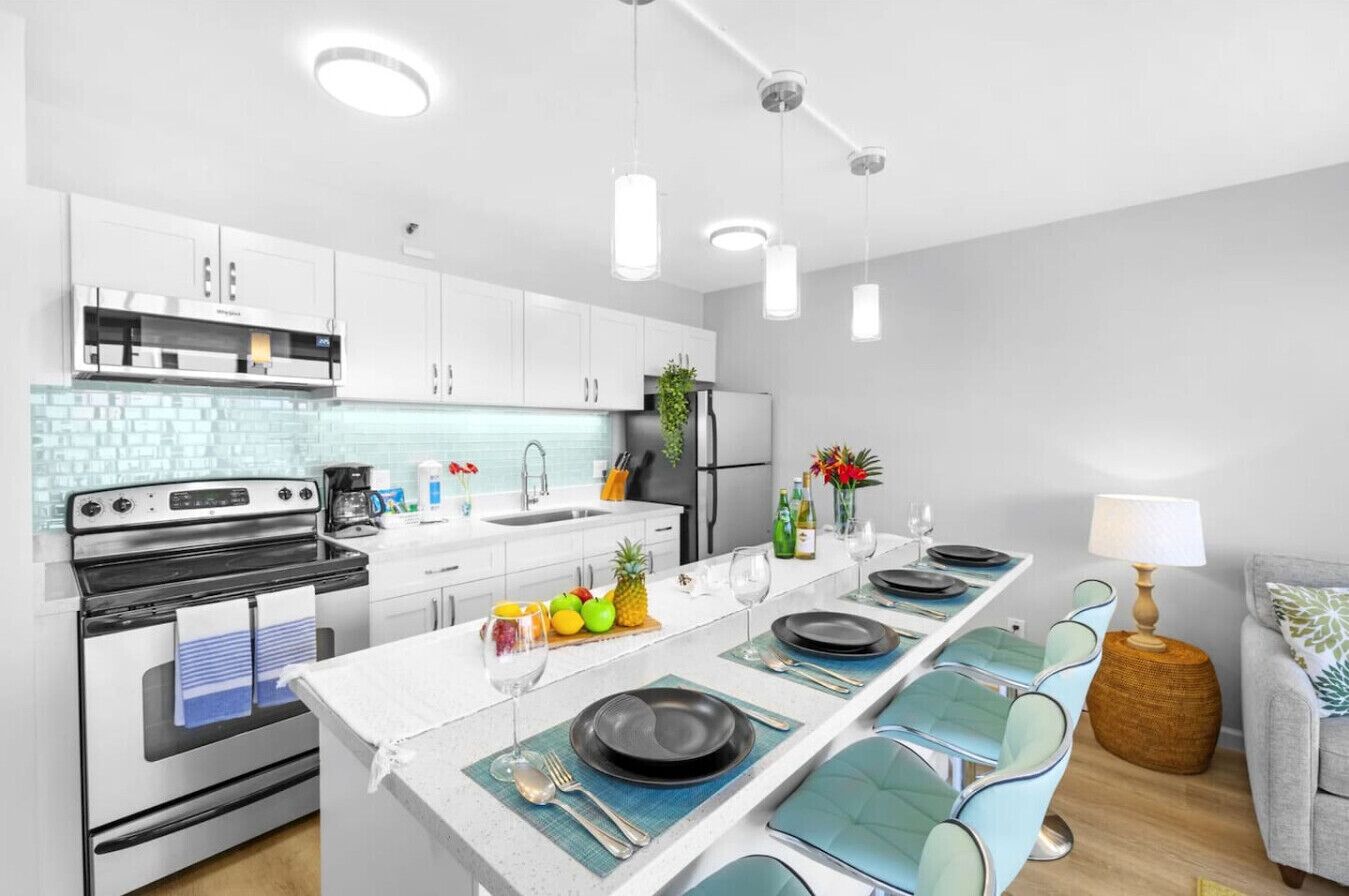 A modern kitchen with white cabinets, a central island with seating, and pendant lighting.