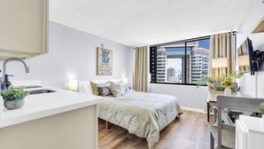 Une chambre d’hôtel moderne équipée d’un lit, d’un petit coin cuisine, d’une table à manger et d’une grande fenêtre donnant sur la ville.