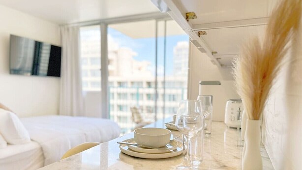 Ett modernt hotellrum med ett matbord i marmor för två personer, en vit soffa och ett stort fönster med utsikt över staden.