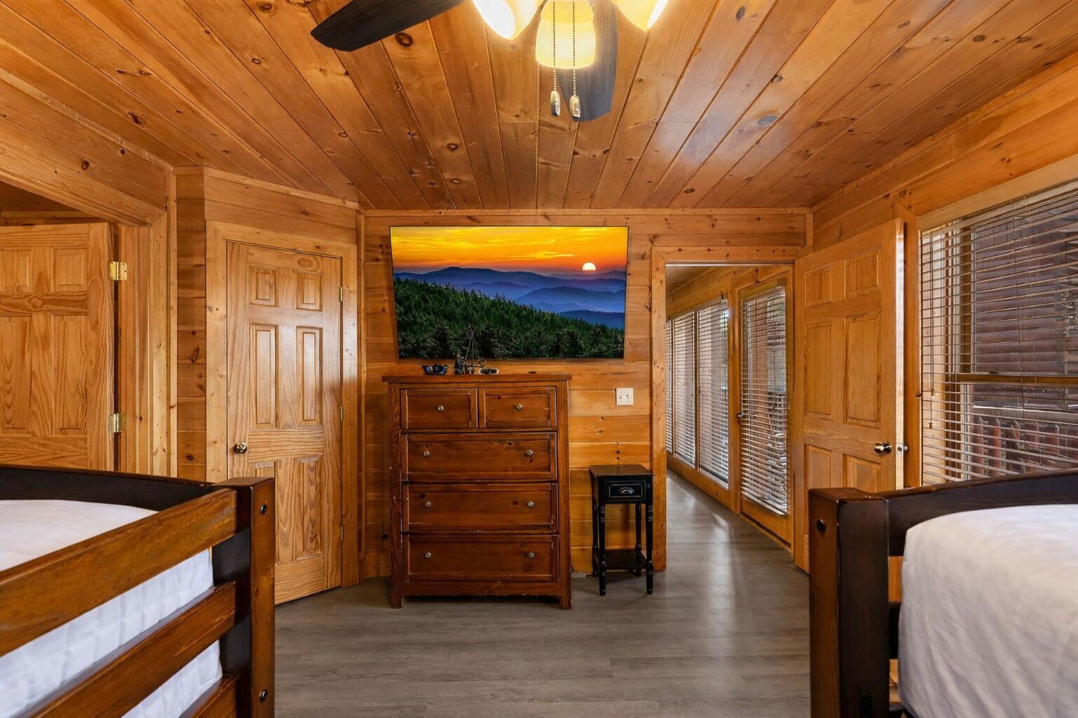 A cabin interior with wooden walls, a bed, a dresser, and a painting of a sunset.
