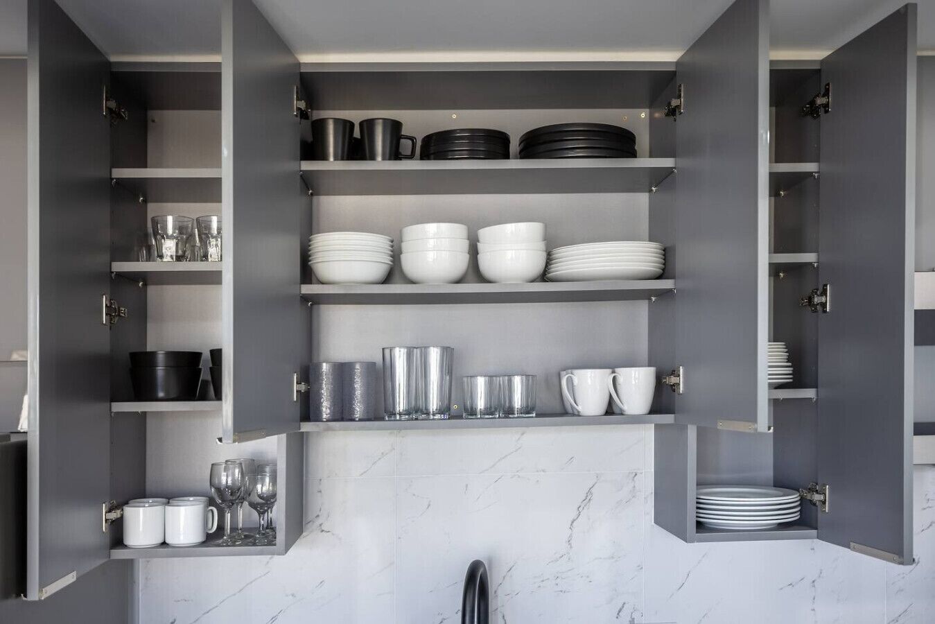 A kitchen with open cabinets displaying various dishes and utensils.