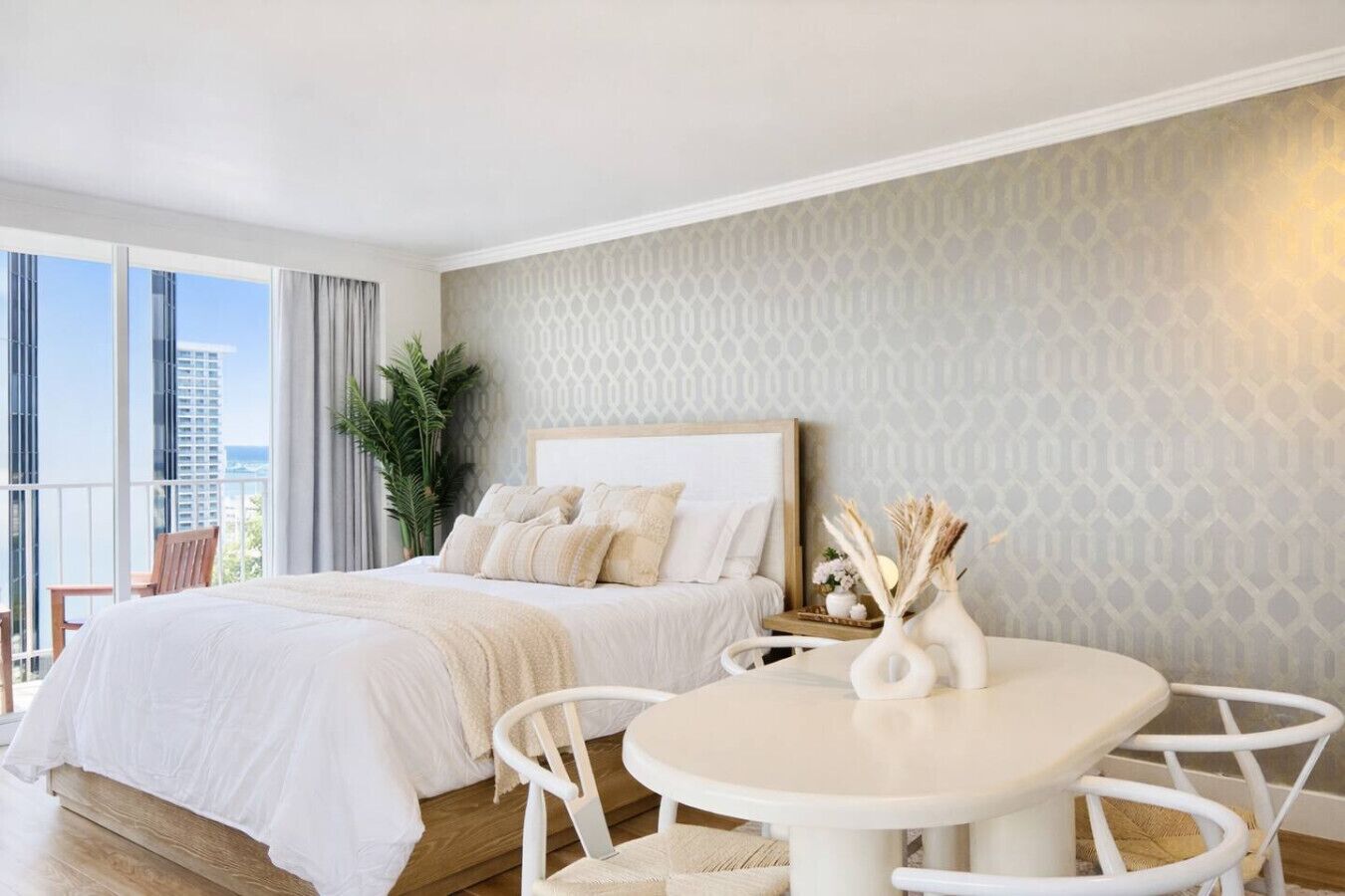 Une chambre d’hôtel moderne dotée d’un grand lit, d’une table de salle à manger ronde et d’un balcon offrant une vue sur la ville.