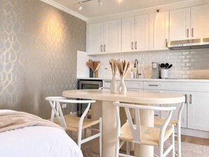 Een moderne keuken met witte kasten, een ronde tafel en twee stoelen.