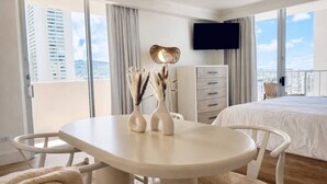Habitación de hotel con balcón, cama, televisor, escritorio y sillas, y cómoda.