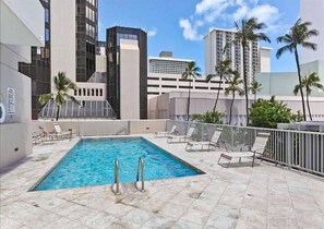 A rooftop pool with lounge chairs, a clear sky, and tall buildings in the background. - Waikiki Gem: Corner Unit with Ocean View 1 Parking (Honolulu)