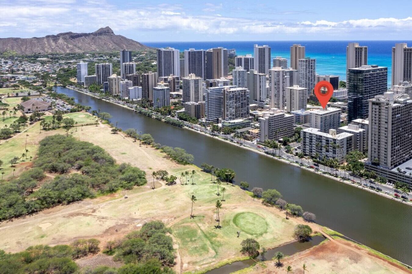 A high-rise urban area with a river running through it, surrounded by greenery and a mountain in the background.