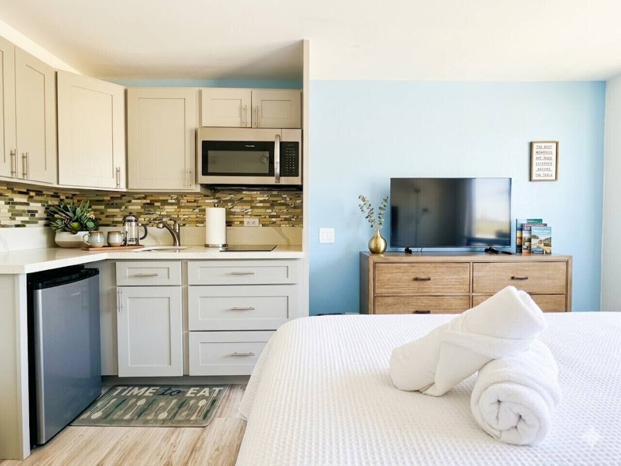 Una habitación de hotel con cama, televisión, microondas, lavamanos y una pequeña cocina.