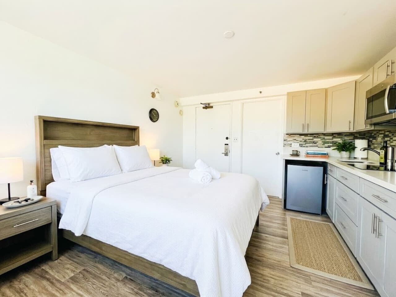 A hotel room with a bed, bedside table, and a kitchenette area.