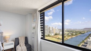 Een moderne kamer met een groot raam, nachtkastje, stoel en uitzicht op een rivier en stadsbeeld.