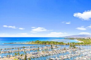 A marina with numerous boats docked, a clear blue sky, and a distant view of a coastline with greenery and buildings. - Waikiki Seaside Escape High Floor (Honolulu)