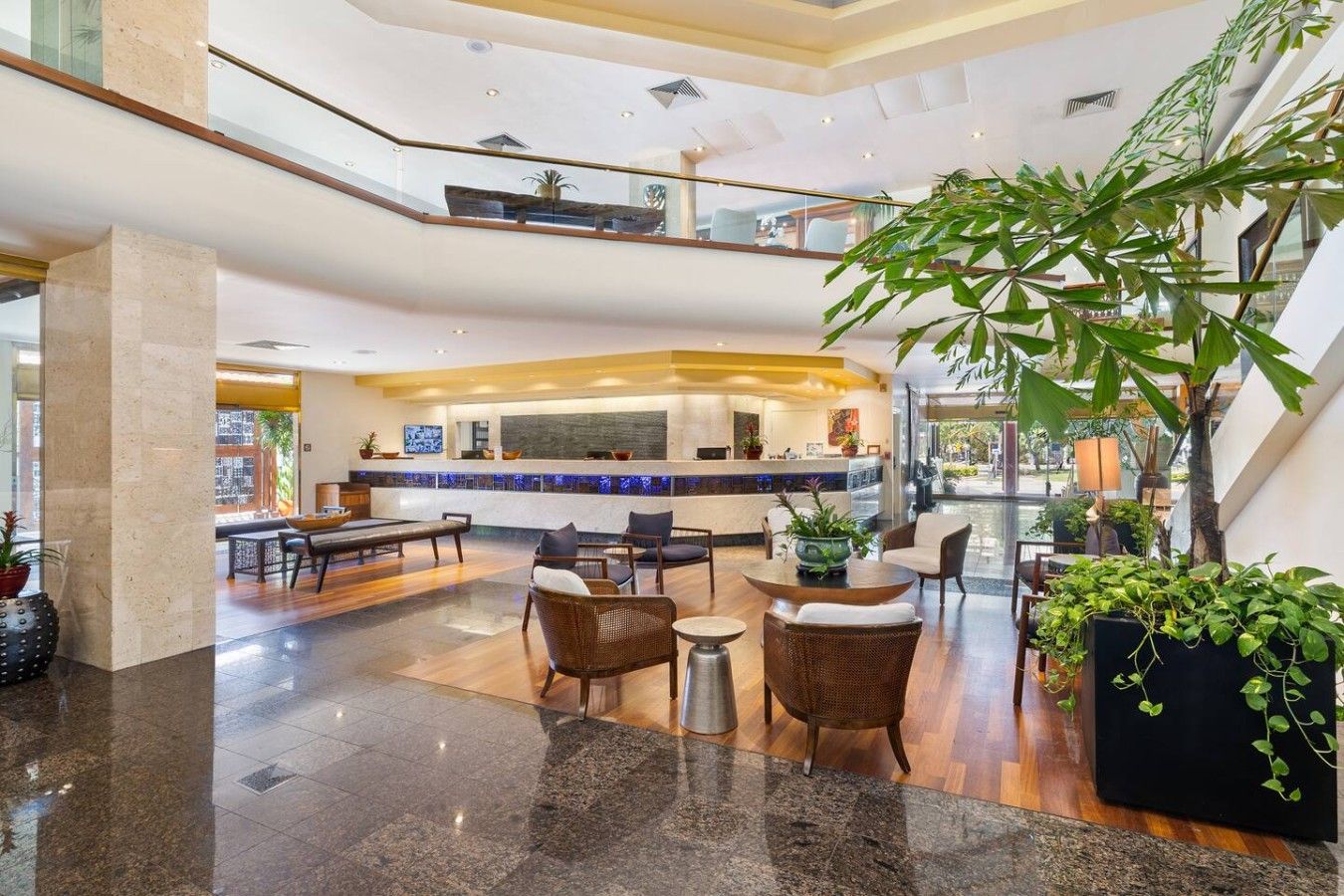 A spacious lobby with a reception desk, seating area, and a large indoor plant.
