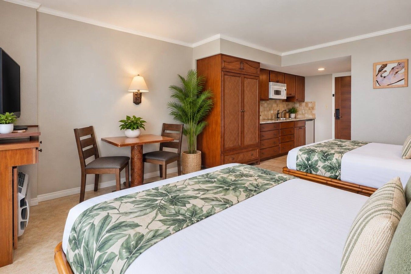 A hotel room with two beds, a dining area, a kitchenette, and a TV.