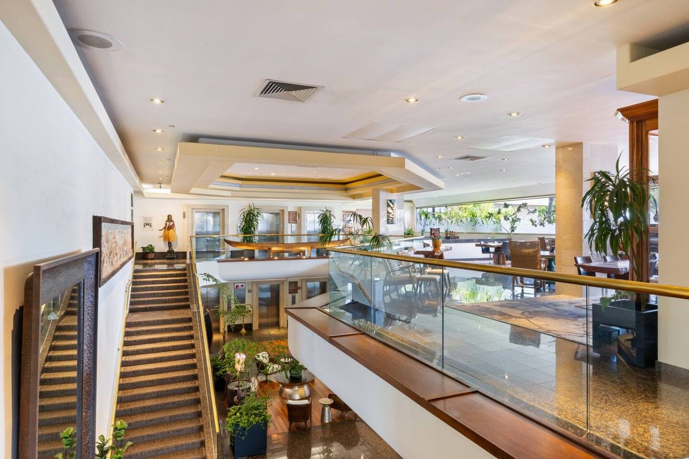 Een hotellobby met meerdere niveaus, een trap, zithoeken en een glazen balustrade met uitzicht op de verdieping beneden.