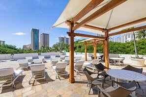 An outdoor patio with lounge chairs and tables, a pergola, and a view of tall buildings. - Unobstructed Ocean View Spacious Studio (Honolulu)