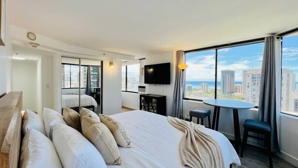 Habitación de hotel con una cama grande, un escritorio, una silla, un televisor y vista a la ciudad.