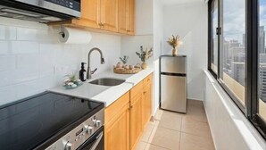 Una cocina moderna con estufa, lavaplatos y refrigerador, armarios de madera y una ventana con vista a la ciudad.