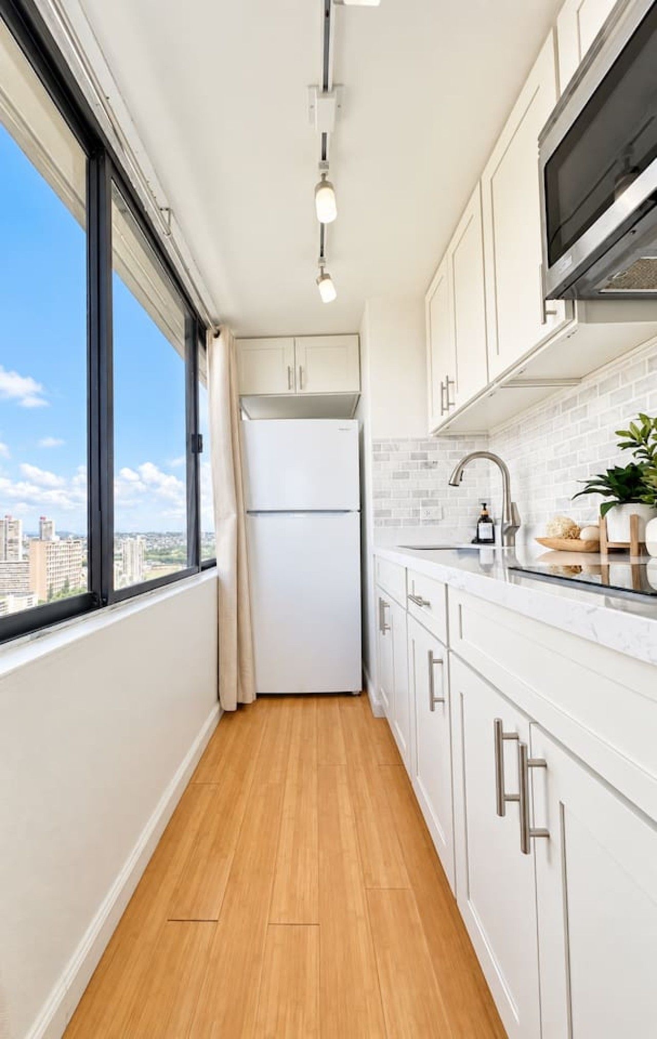 A narrow kitchen with a view of the city, a refrigerator, a sink, and a window.
