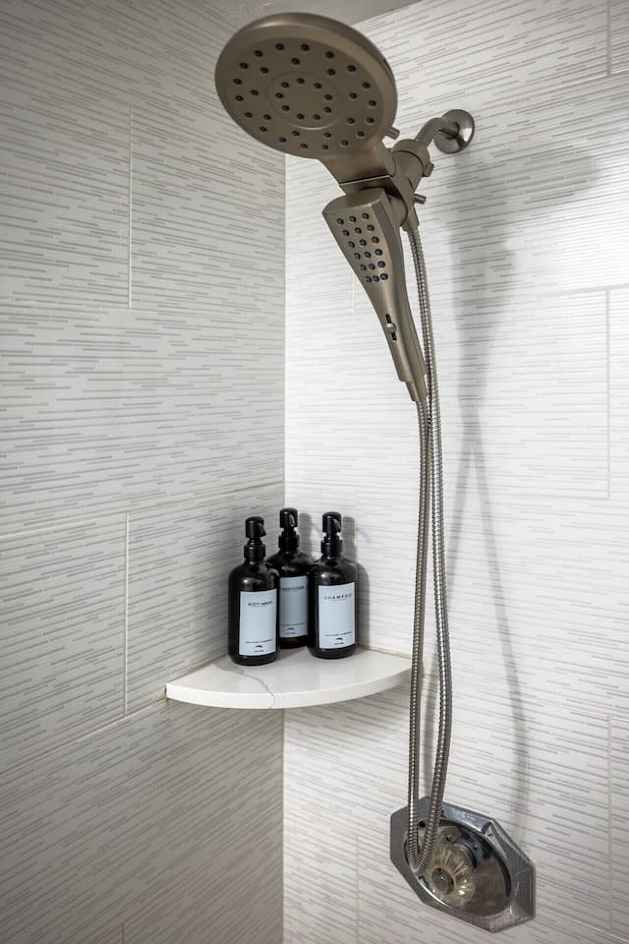 A modern shower with a rain showerhead and handheld showerhead, mounted on a wall with a built-in shelf holding three bottles of shampoo.