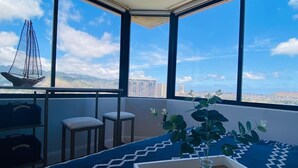 Ein Eckzimmer mit großen Fenstern, einem blauen Teppich, einer Pflanze und einem kleinen Tisch.