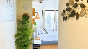 Een hal die leidt naar een slaapkamer met een bed, een kamerplant, een wandklok en een decoratieve bladwand.