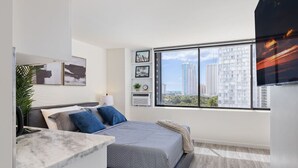 Una camera da letto moderna con un'ampia finestra, un letto, un comodino e vista sui grattacieli.