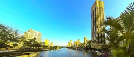 Une rivière bordée de bâtiments des deux côtés, un ciel dégagé et quelques espaces verts au premier plan.