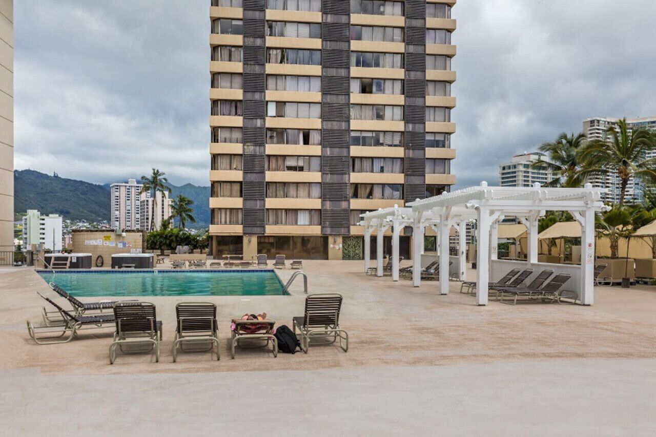 A hotel pool area with a large pool, lounge chairs, and a white pergola structure.