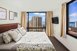 A hotel room with a large bed, a TV, and a view of the city and ocean. - Waikiki Beach Ocean View 1 BD +Lanai +FREE parking (Honolulu)
