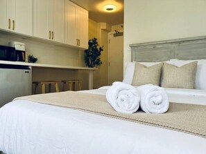 A hotel room with a bed, a bedside table, a microwave, and a plant. - Cozy Studio at the Heart of Waikiki (Honolulu)