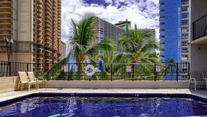 A swimming pool with a view of tall buildings and palm trees. - PW9F-23 Modern Cozy Waikiki Studio Across Hilton Village 9 (Honolulu)